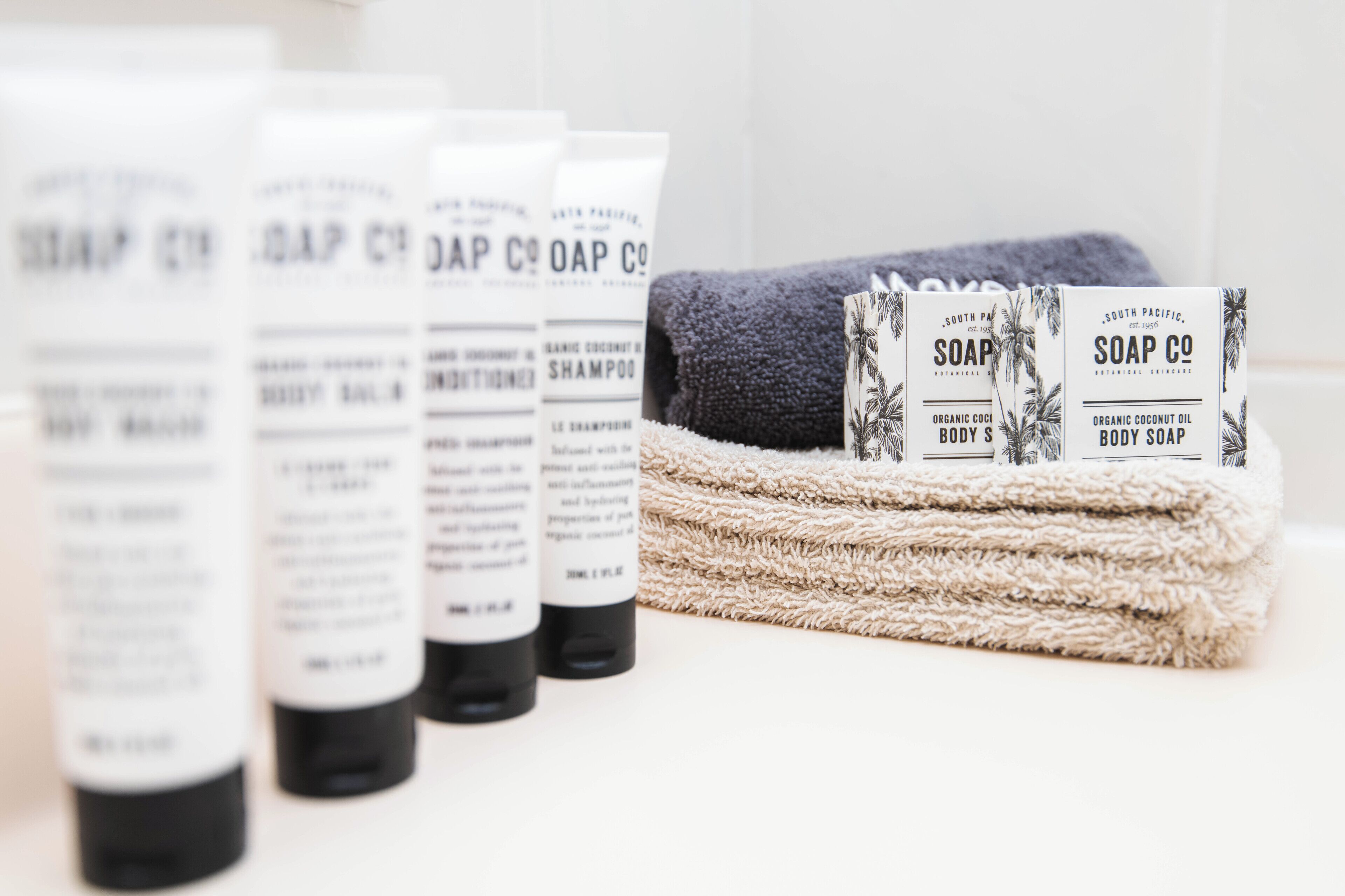 A row of toiletries including shampoo and body soap bottles, with a folded towel in the background.