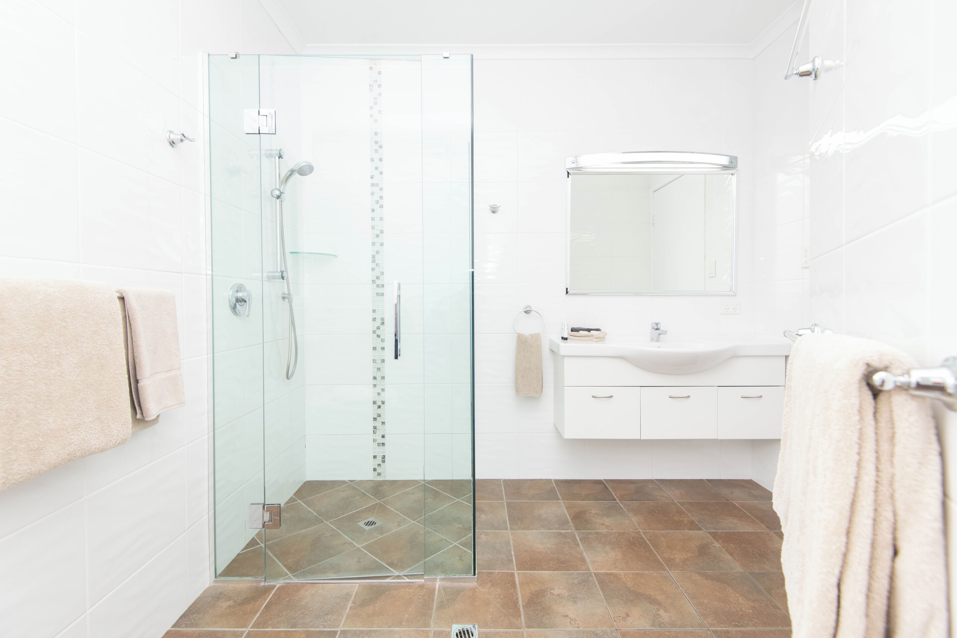 A modern bathroom with a glass-enclosed shower, white tiles, a sink with a mirror, and a towel rack.