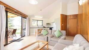 A modern living room with a sofa set, a wooden coffee table, and a kitchen area with a microwave and stove. - Whispering Pines (Norfolk Island)