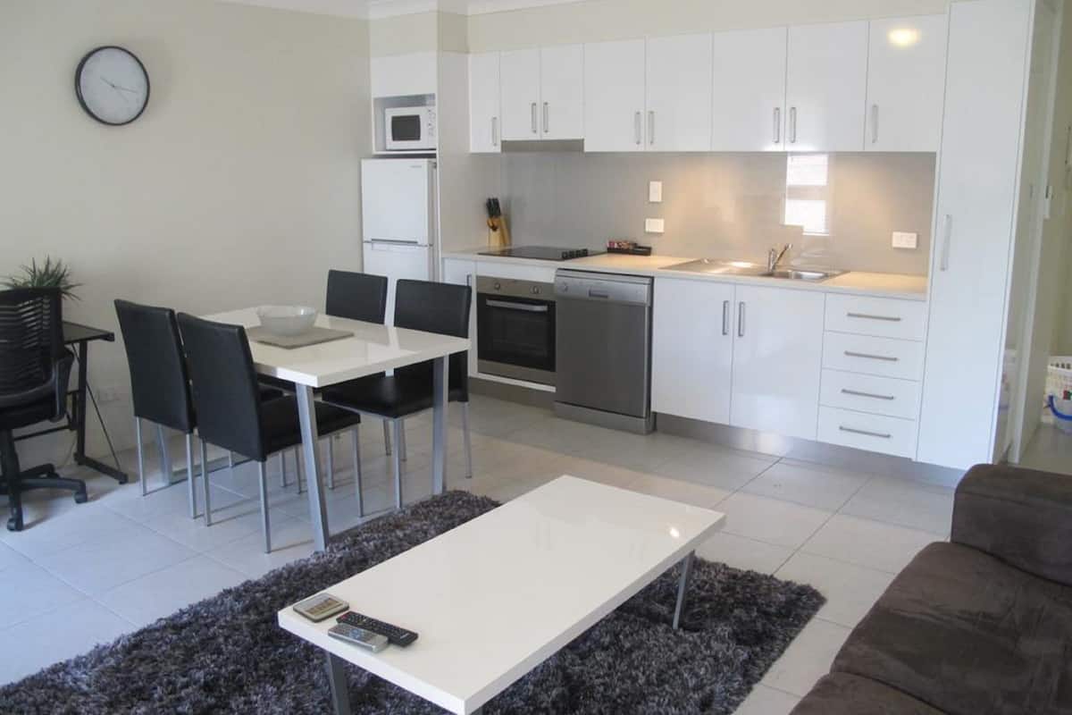 A modern kitchen with white cabinets, a microwave, oven, and dishwasher. There is a dining table with chairs and a coffee table in the living area.