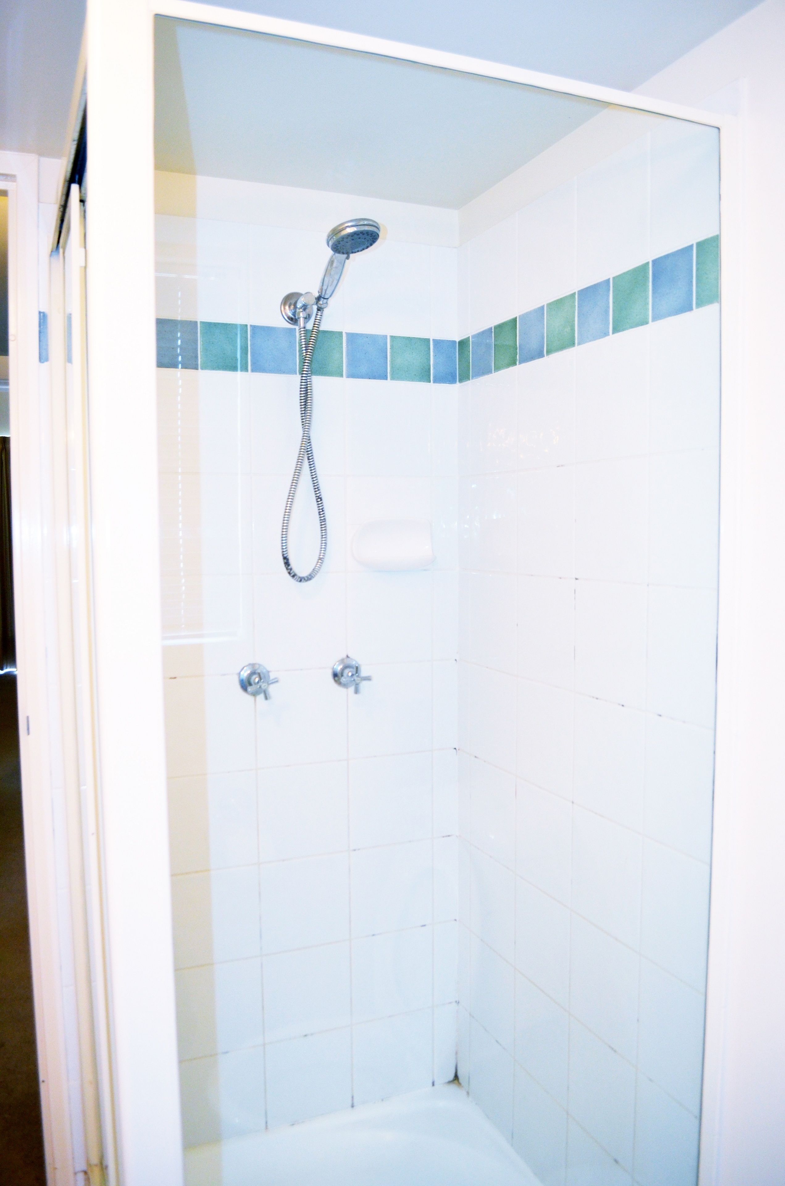 Une douche équipée d’un pommeau de douche à main et de deux robinets fixés au mur.
