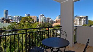 Varanda com vista para a cidade, com mesa e cadeiras, e corrimão.