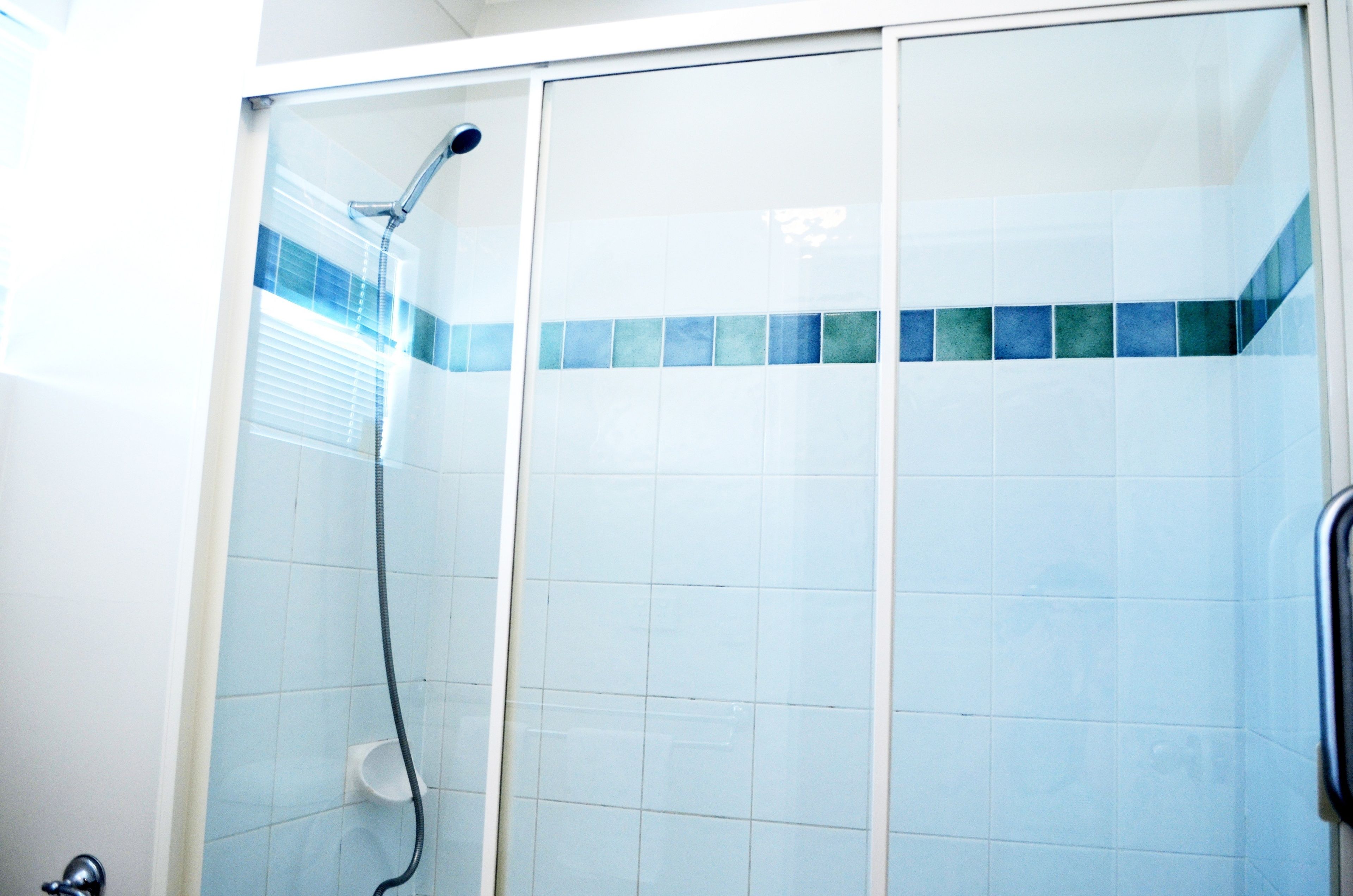 A shower with a glass door, a handheld showerhead, and a small white container on the wall.