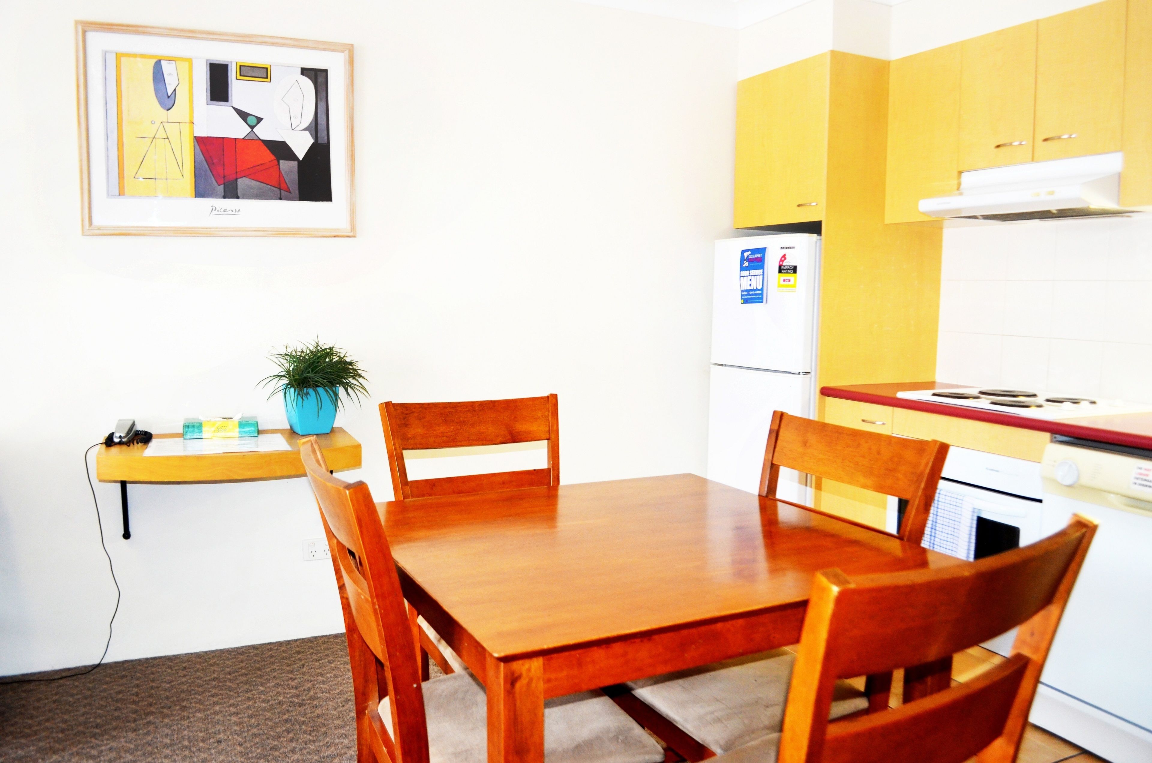 A compact kitchen with a wooden table and chairs, a small countertop with a plant, and a refrigerator.