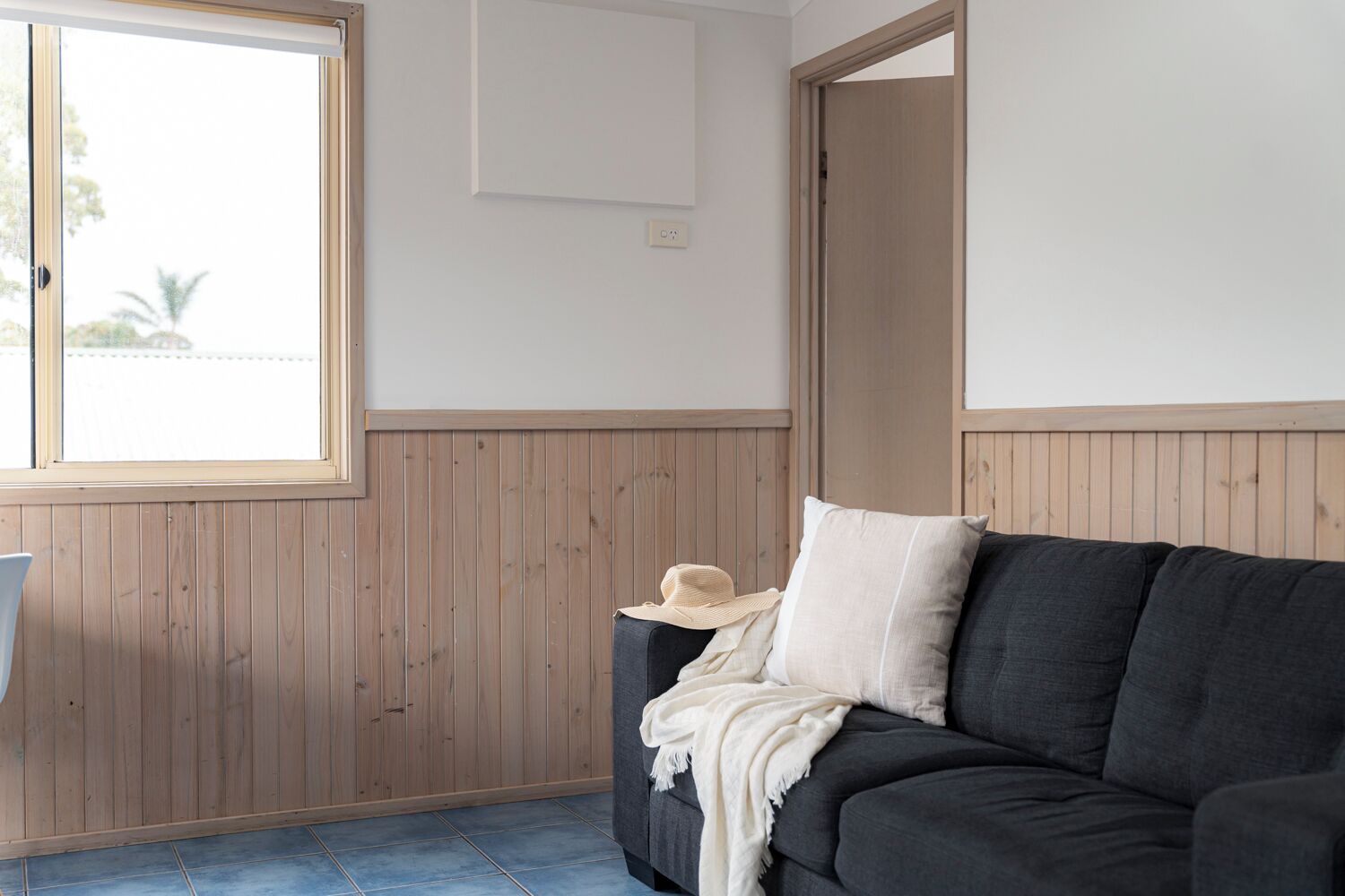 Una habitación con un sofá gris oscuro, una pared blanca y una pared revestida de madera.