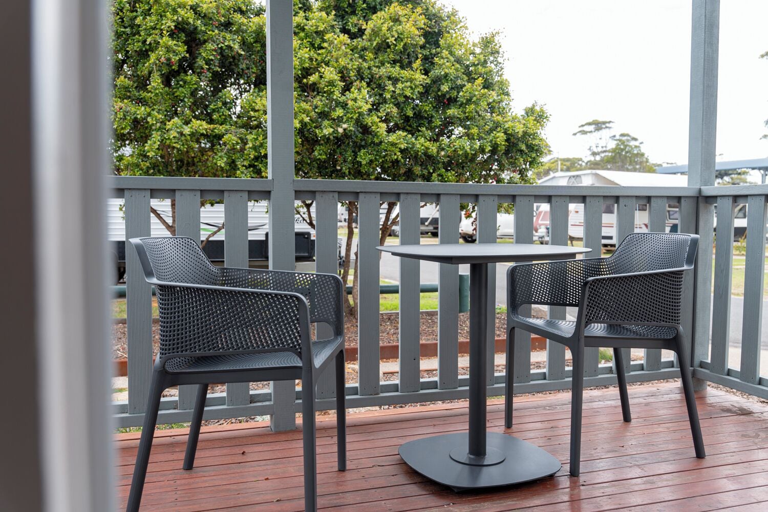 Un espace extérieur abrité, aménagé avec deux chaises en métal et une table, entouré d’une terrasse en bois et d’une rambarde en métal.