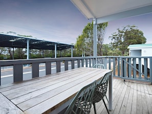 A wooden deck with a table and chairs, a covered area with a metal roof, and a view of trees and a road. - The Black Dolphin Holiday Park (Merimbula)