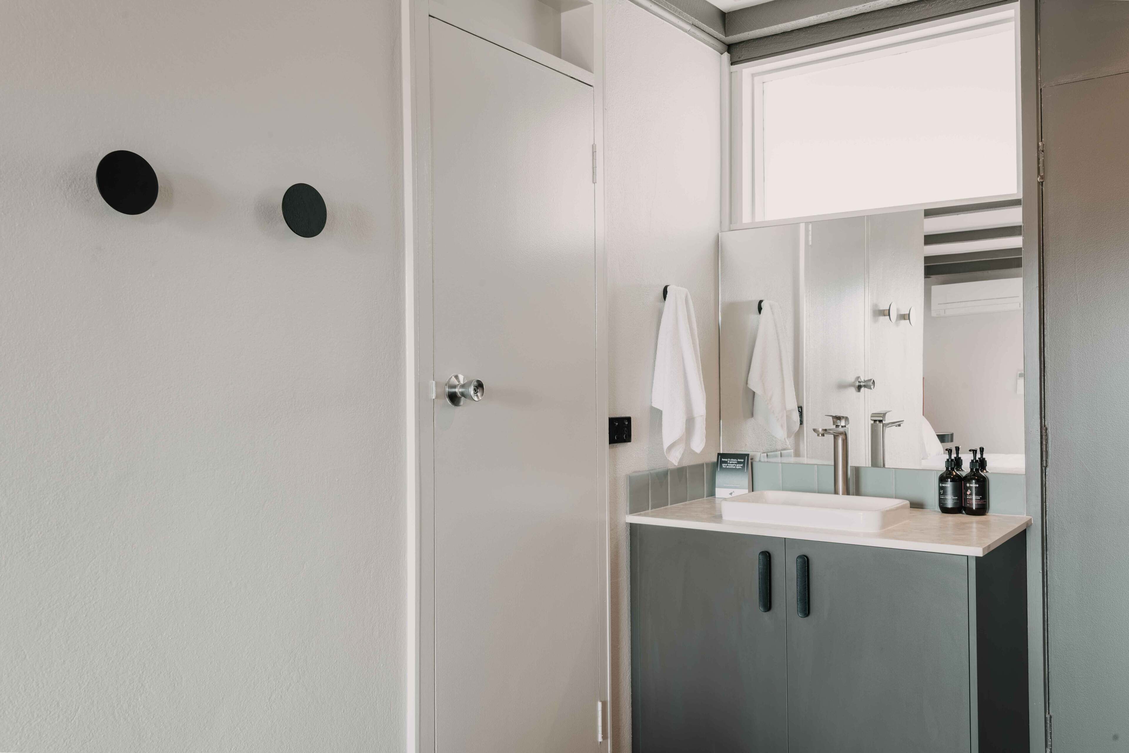 A bathroom with a white door, a mirror, a sink, and two black circular objects on the wall.