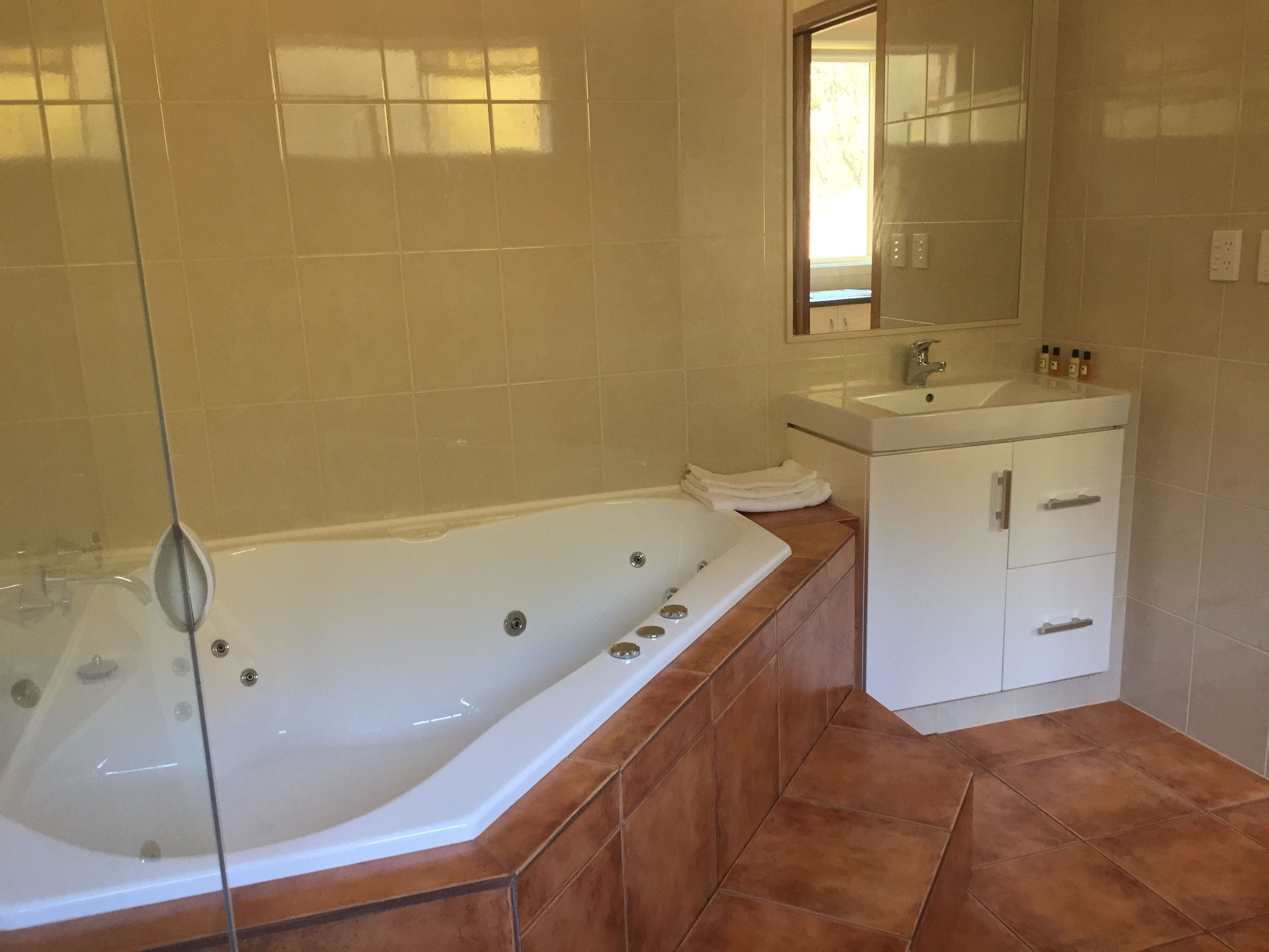 A bathroom with a glass-enclosed bathtub, a white vanity with a sink, and a mirror above the vanity.