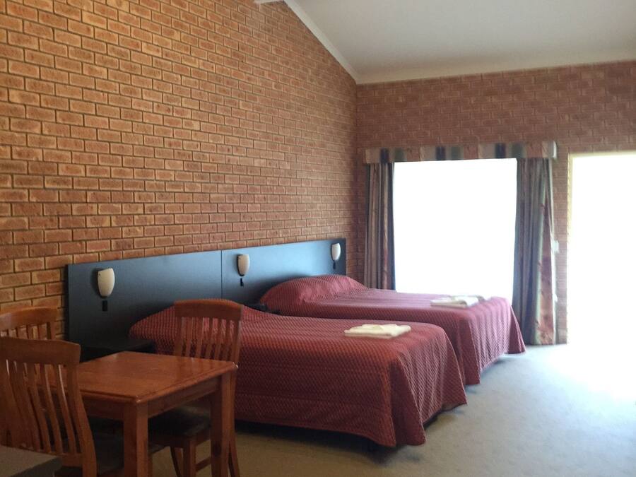 Ein Hotelzimmer mit zwei Betten, einer Ziegelwand, einer runden Deckenleuchte und Blick nach draußen.