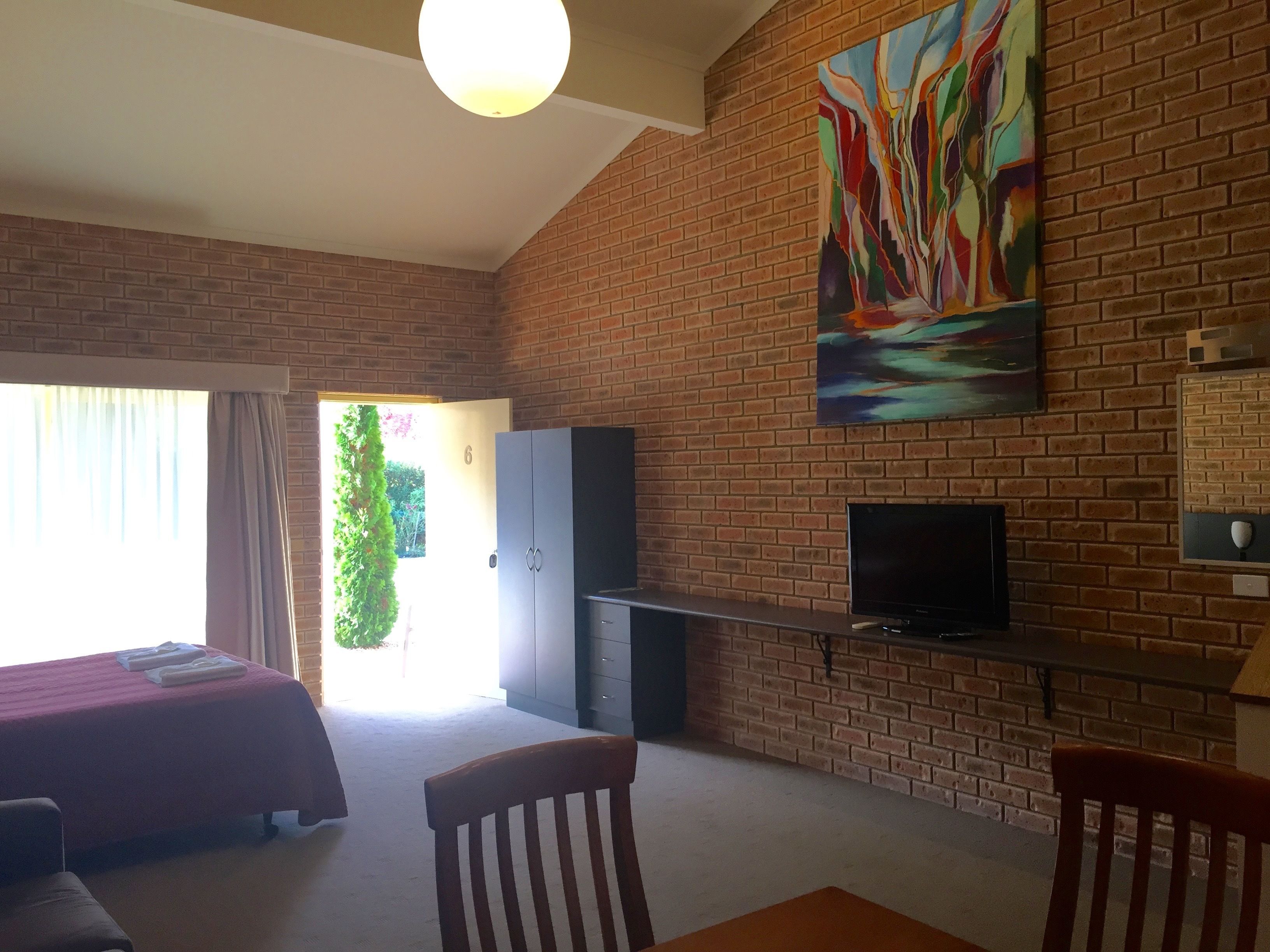A room with a brick wall, a painting, a TV, a bed, and a desk.