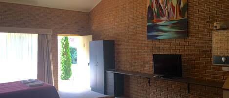 A room with a brick wall, a painting, a TV, a bed, and a desk.