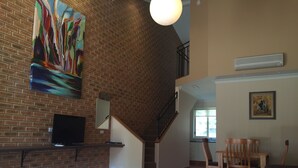 Une chambre d’hôtel avec un mur en briques, un tableau, une télévision, un lit avec des serviettes, un escalier et un coin repas.