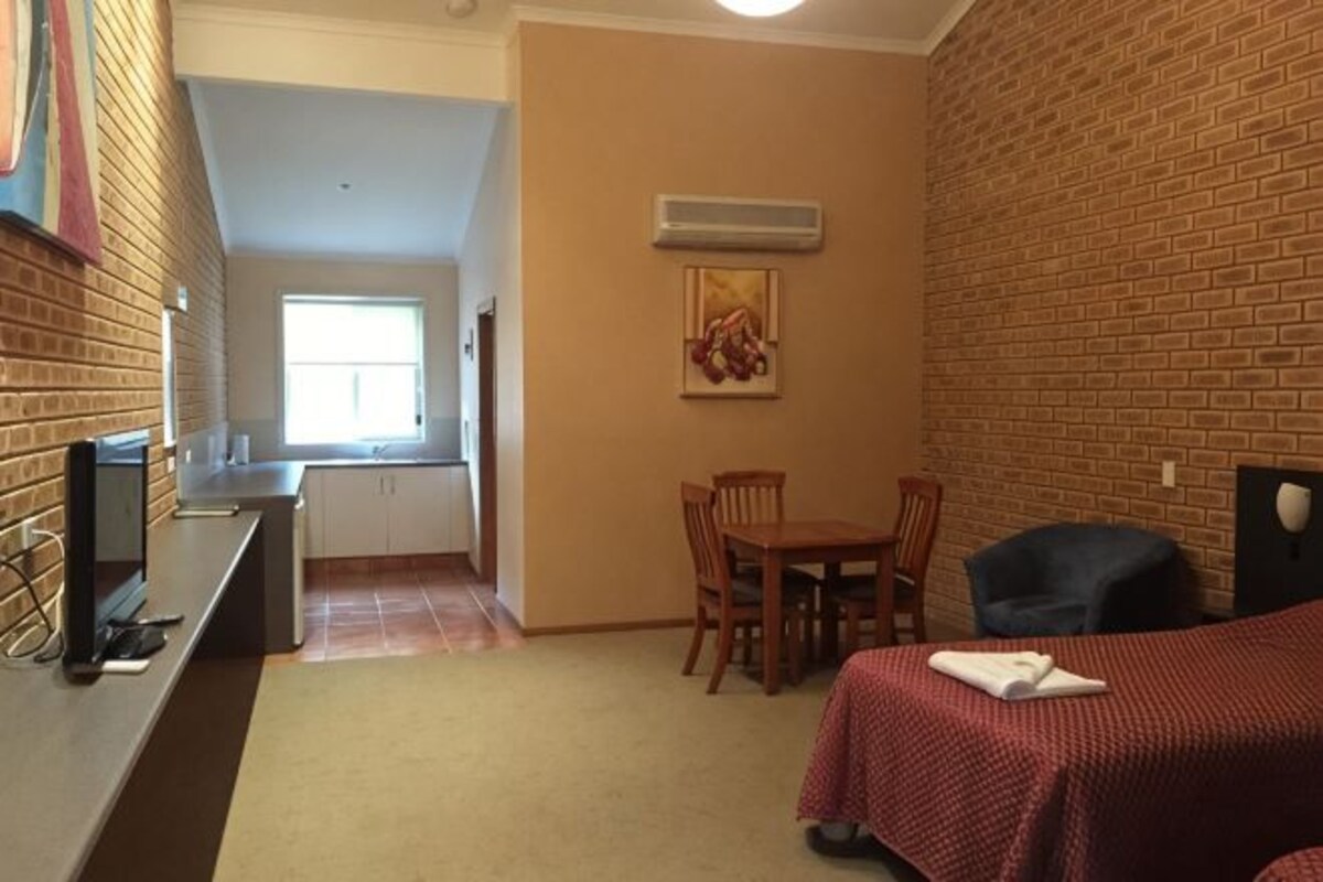 A compact hotel room with a kitchenette, a dining area, and a bed.