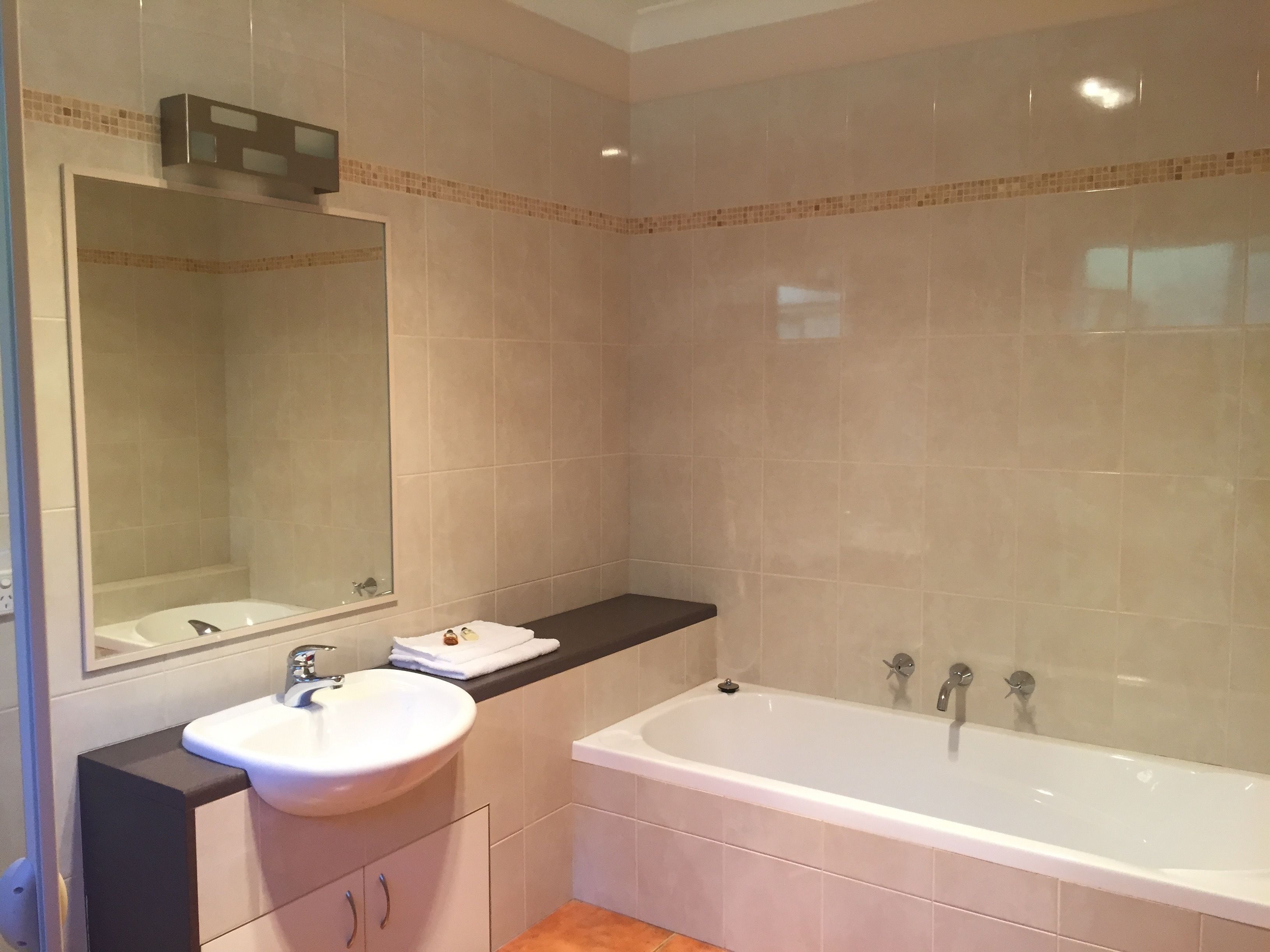 A bathroom with a white sink, a mirror, a bathtub, and beige tiled walls.