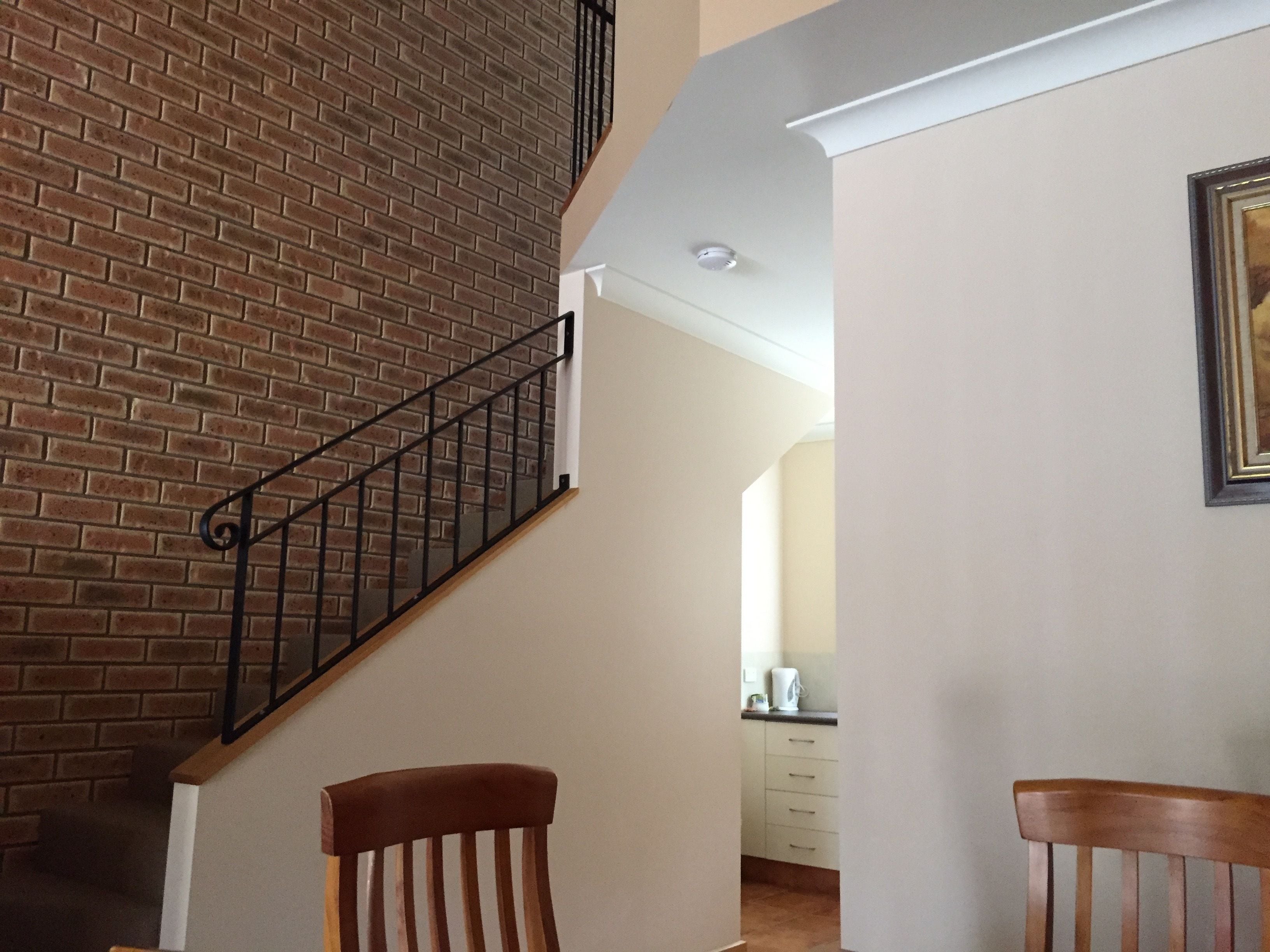 Una escalera con un muro de ladrillo, una silla de madera y una cocina al fondo.