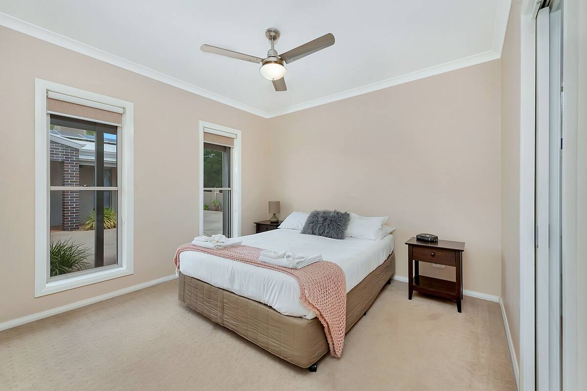 A bedroom with a large bed, a ceiling fan, two bedside tables, and a window with a view of a building.