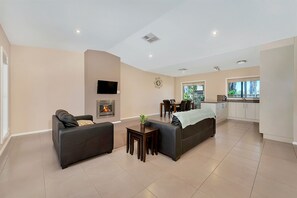 A modern living room with a fireplace, a dining area, and a kitchen. - Kennedy Holiday Villas (Mulwala)