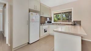 Una cocina moderna con armarios blancos, un refrigerador, un microondas, un horno y un ventanal con vistas al verdor.