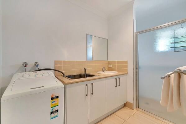 A compact kitchen with a washing machine, a sink, and a glass shower enclosure. - Kennedy Holiday Villas (Mulwala)