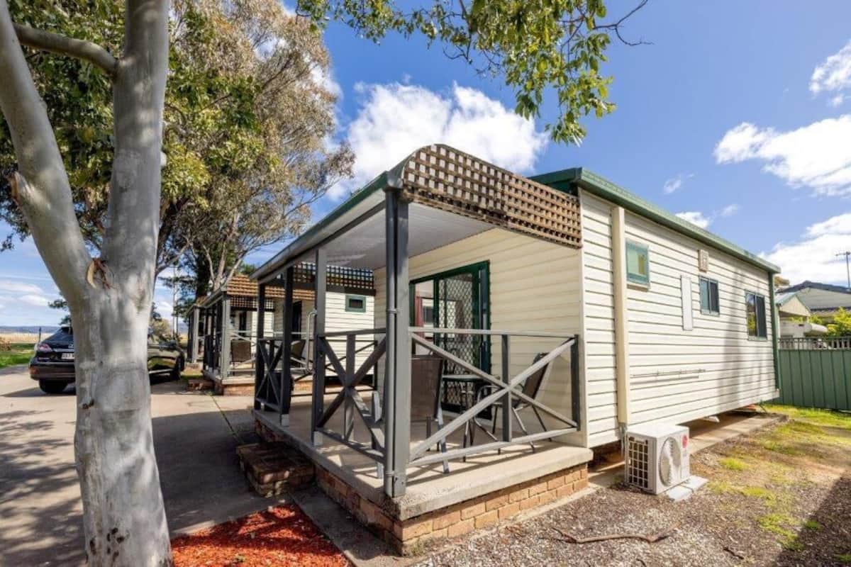 A mobile home with a covered porch, a brick foundation, and a small garden area.