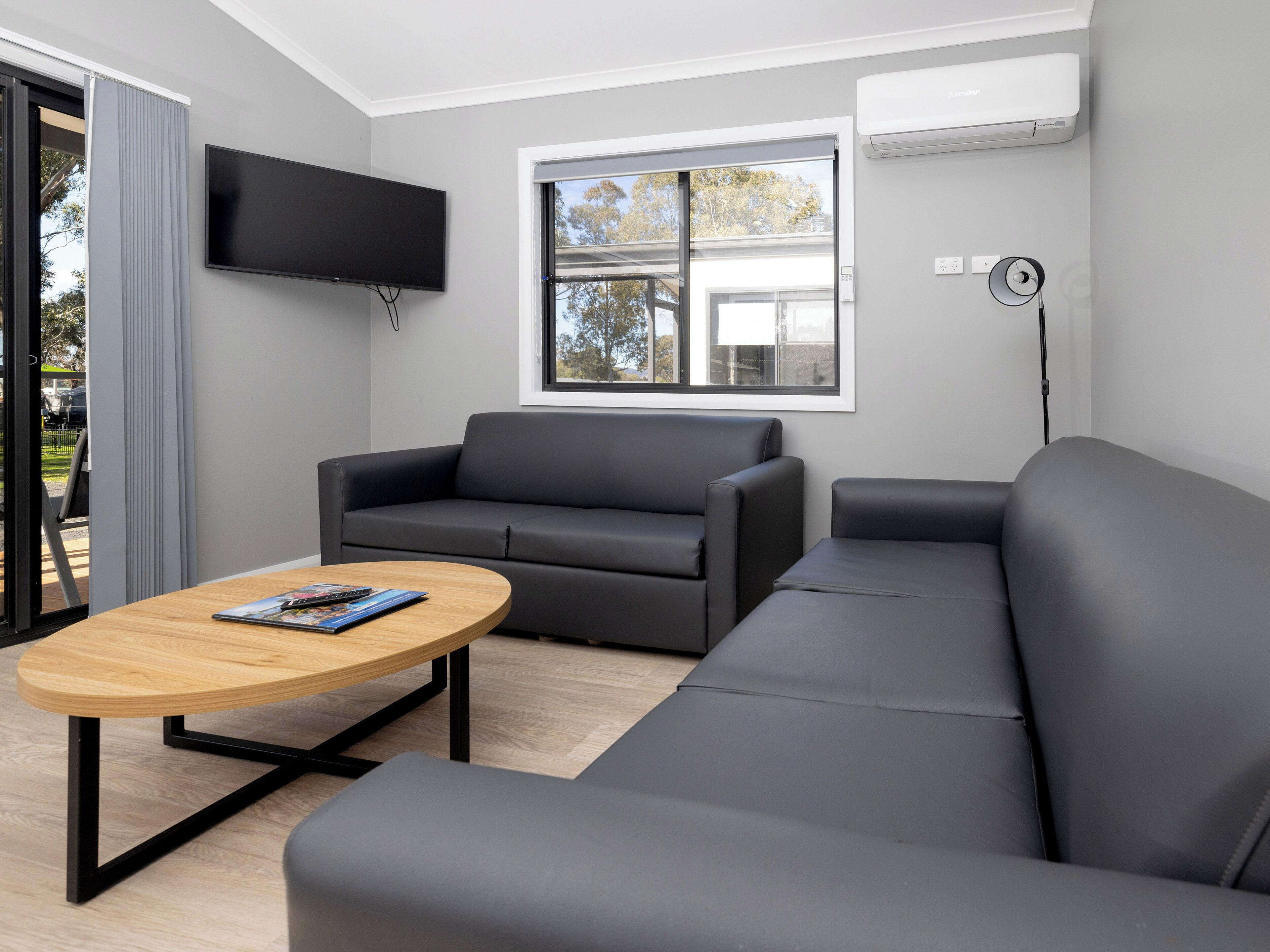 A modern living room with a grey sofa, a wooden coffee table, and a flat-screen TV mounted on the wall.