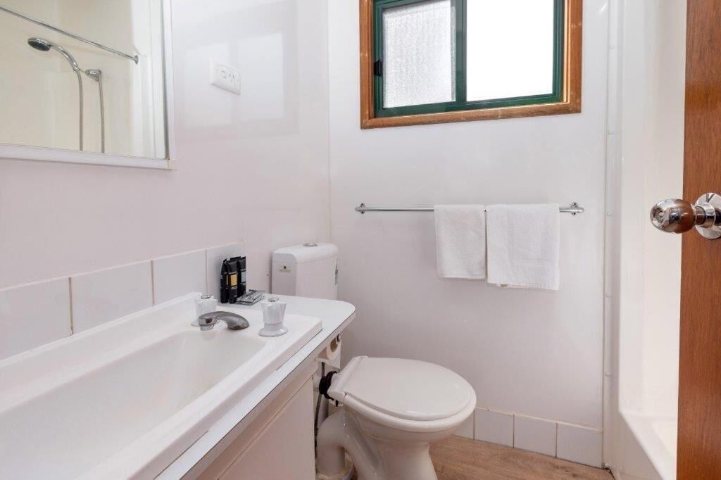 Un baño con una bañera blanca, un inodoro y una ventana sobre el inodoro.