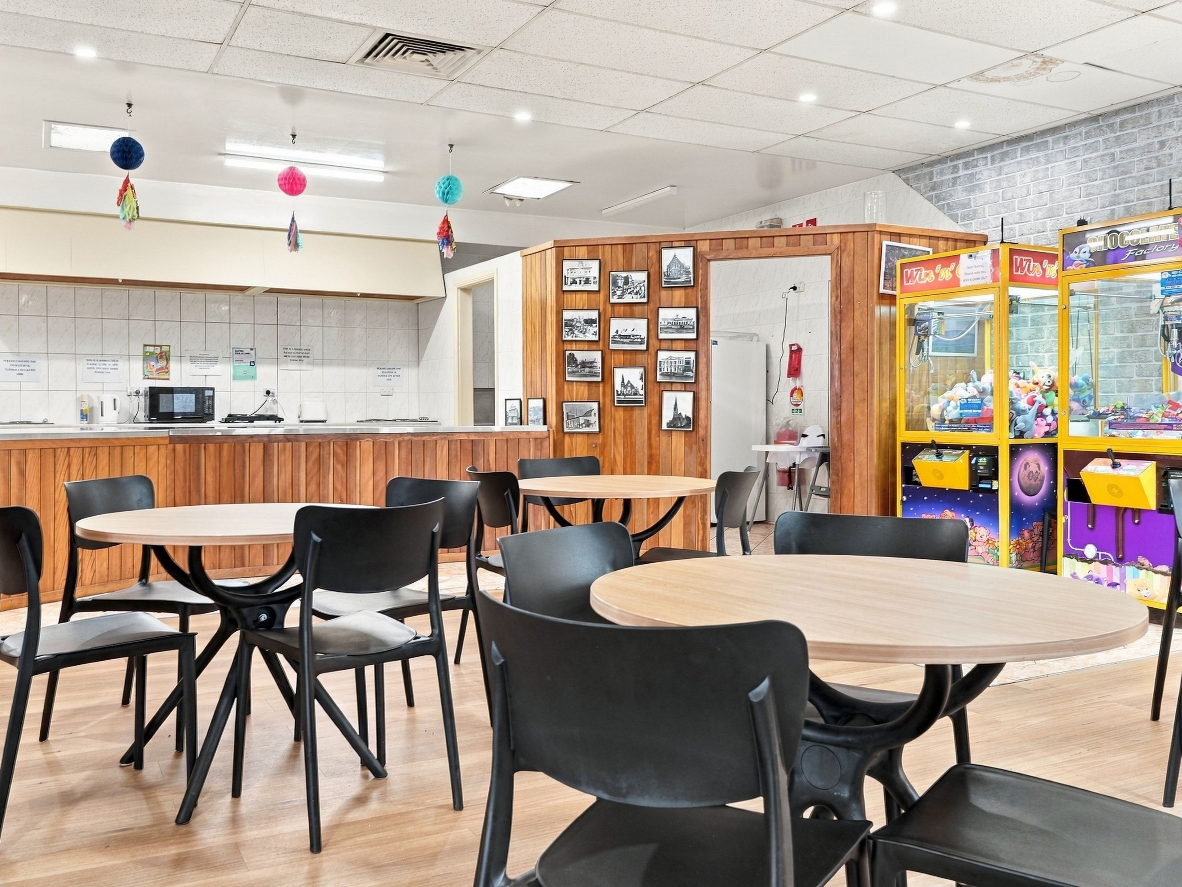 Ein Restaurantinnenraum mit Holztischen und -stühlen, einer Theke mit Mikrowelle und einer Wand mit gerahmten Bildern.