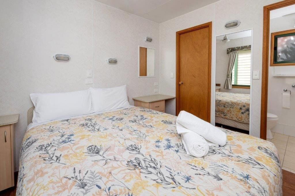 A bedroom with a floral bedspread, a wooden door, a bedside table, and a mirror on the wall.