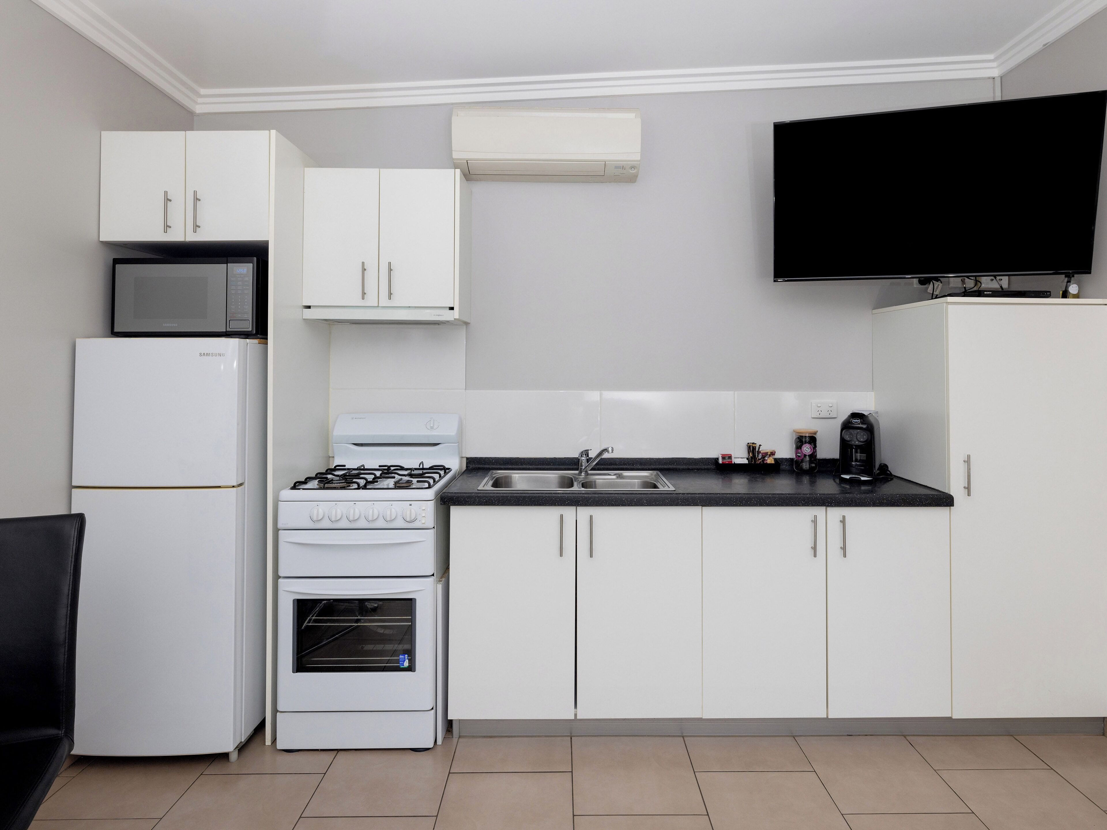 A modern kitchen with white cabinets, a built-in microwave, a gas stove, a sink, and a flat-screen TV mounted above the counter.