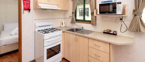 A compact kitchen with a gas stove, oven, and microwave, wooden cabinets, a sink, and a window with curtains.
