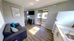 Eine moderne Wohnung mit einem grauen Sofa, einem Essbereich, einer Küche mit Spüle und einer Schiebeglastür nach draußen.