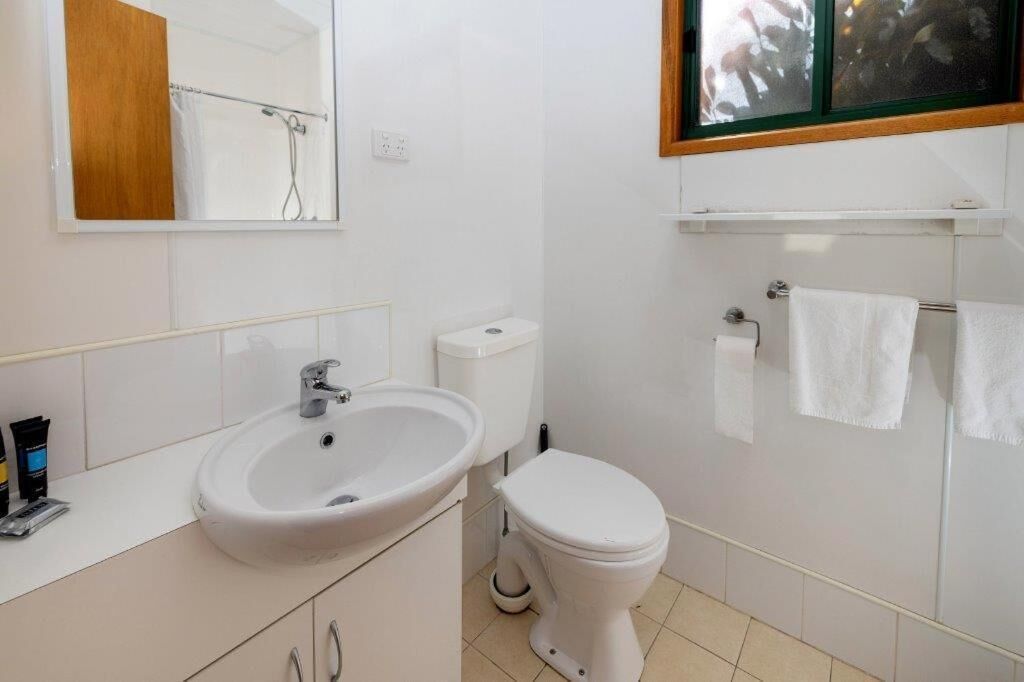 Une salle de bain avec un lavabo blanc, des toilettes et un miroir au-dessus du lavabo.