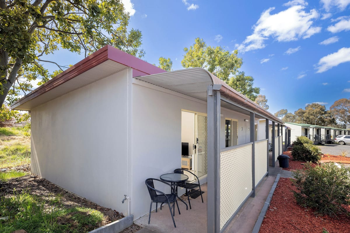 A single-story mobile home with a covered patio area, a small table with chairs, and a view of the surrounding landscape.