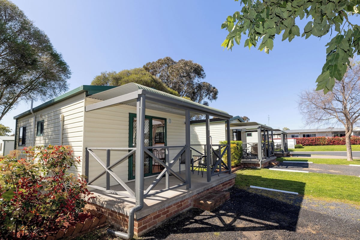 A row of mobile homes with a covered patio area, a brick foundation, and a grassy lawn.