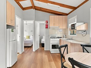 A modern kitchen with wooden cabinets, a white stove, and a dining area with a table and chairs. - BIG4 Mudgee Holiday Park (Mudgee)