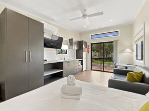 A modern hotel room with a bed, a flat-screen TV, a kitchenette, and a sliding glass door to the outside. - BIG4 Mudgee Holiday Park (Mudgee)