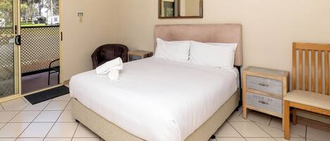A hotel room with a large bed, a wooden nightstand, a chair, and a sliding glass door leading to an outdoor area.