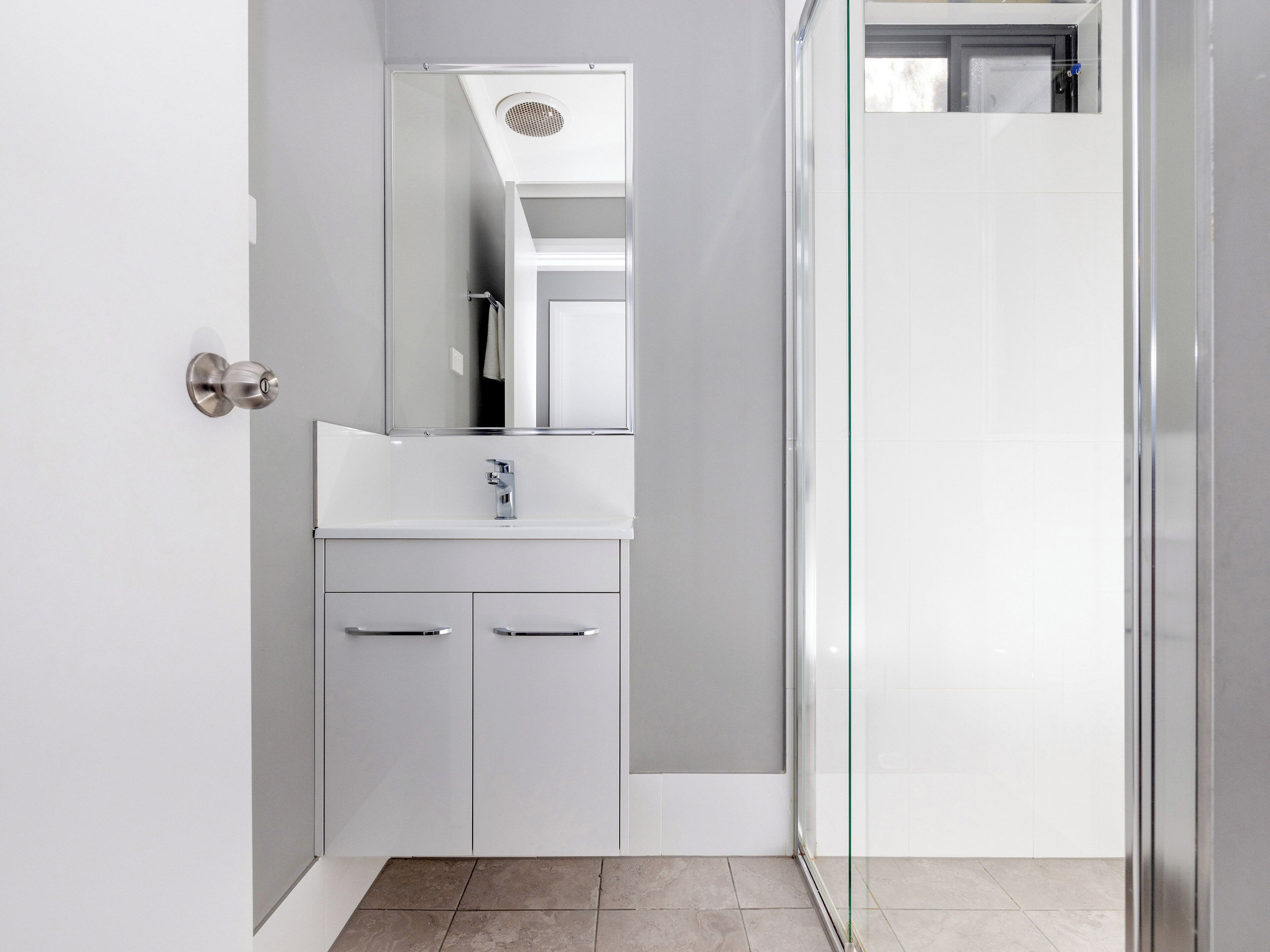 A modern bathroom with a glass shower enclosure, a white vanity with a mirror, and a door with a round handle.