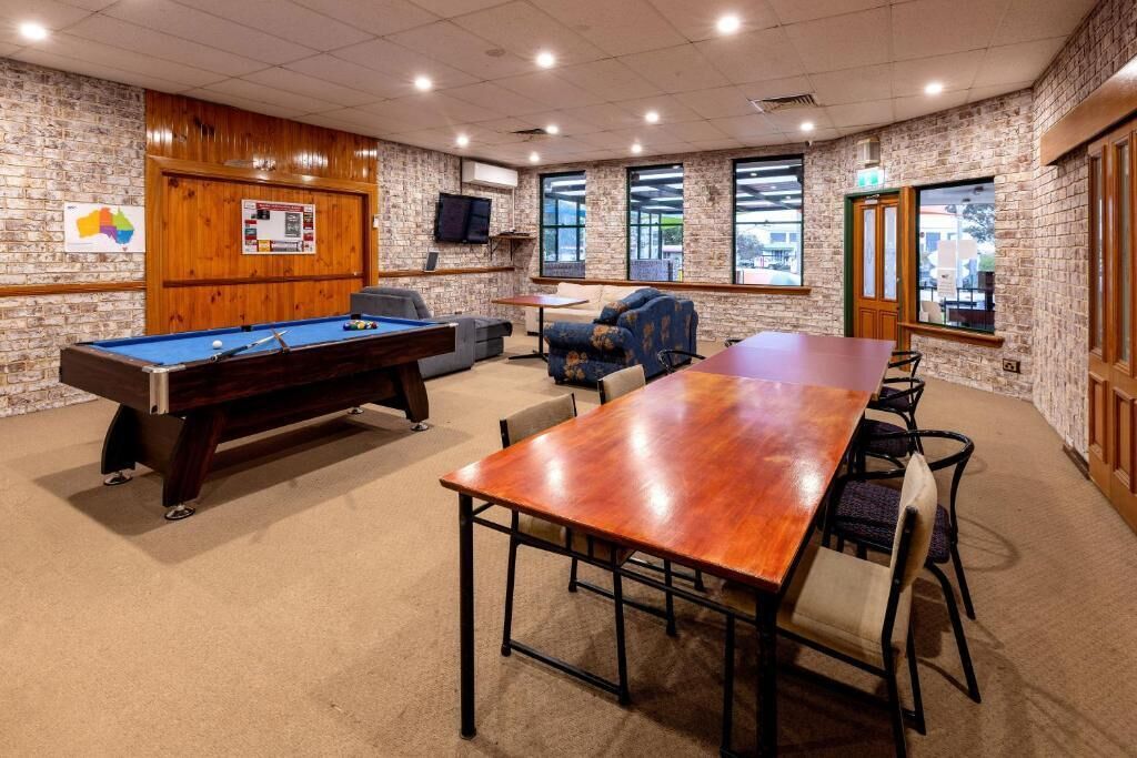 A room with a pool table, a long table with chairs, a sofa, and a brick wall.