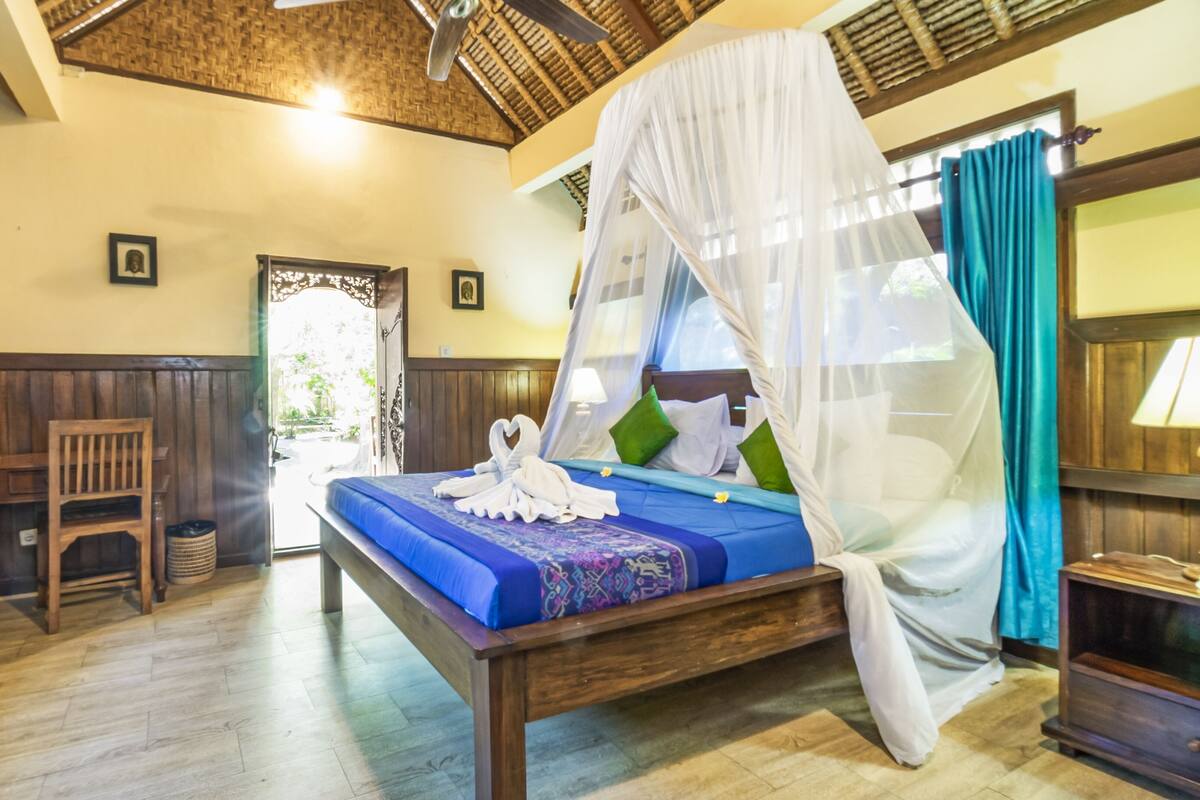 A room with a bed, wooden furniture, a ceiling fan, and a view through a doorway.