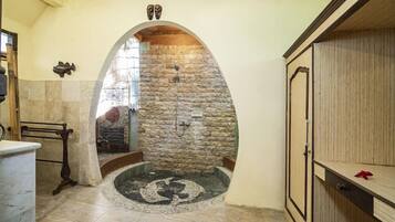 A stone-walled bathroom with a circular mosaic floor, a wooden bench, and a cabinet with a drawer.