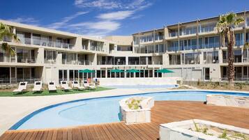 A hotel with a swimming pool, multiple balconies, and a palm tree.