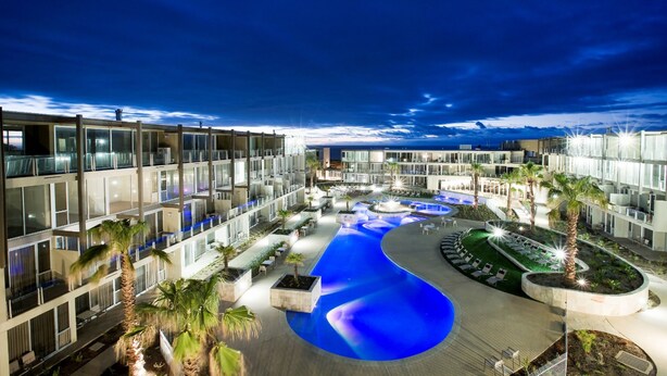 A modern hotel with a swimming pool, palm trees, and a well-lit outdoor area. - Onshore Torquay (Torquay)