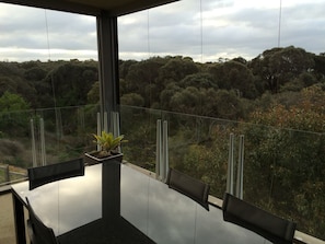 Een moderne eethoek buiten met een glazen tafel en stoelen, met uitzicht op een bebost landschap.