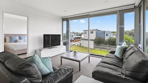 A modern living room with a sofa, a coffee table, a TV, and a large window offering a view of the outside. - Onshore Torquay (Torquay)