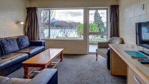 A hotel room with a sofa, a wooden table, a desk with a computer, and a TV. - Lakeside Motel - Queenstown (Queenstown)