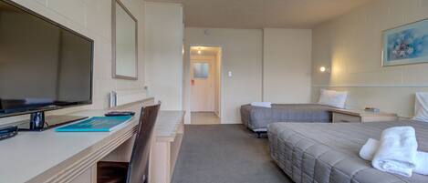 A hotel room with a desk, a bed, a TV, and a painting on the wall.