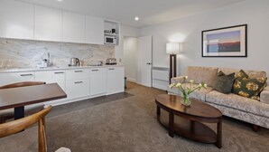 A modern kitchen with white cabinets, a marble countertop, and a dining area with a wooden table and chairs. - Lakeside Motel - Queenstown (Queenstown)