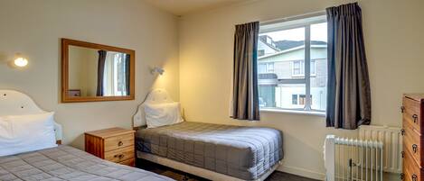A bedroom with two beds, a dresser, a radiator, and a window with curtains.
